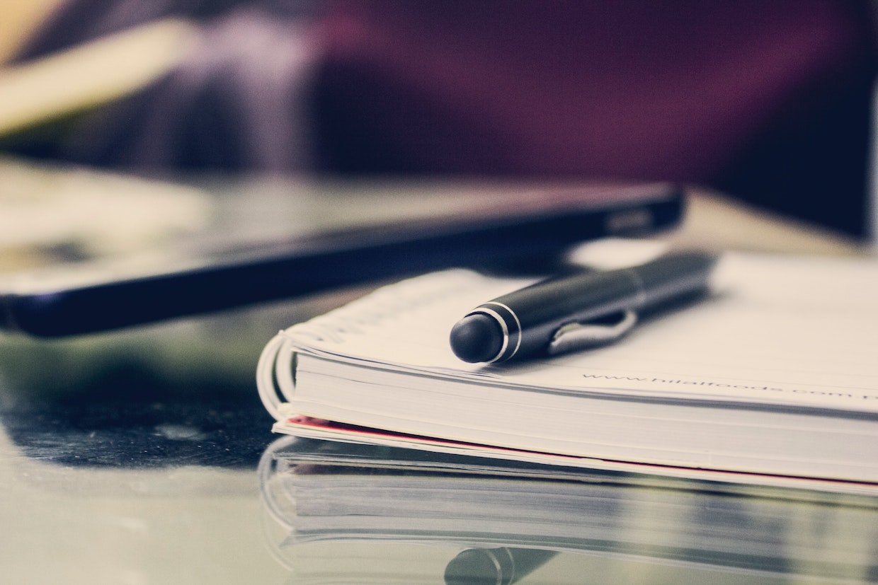 Image of a notebook and pen on a desk.